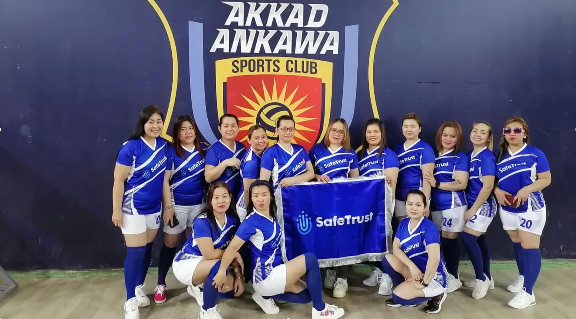 SafeTrust-sponsored Filipino expatriate volleyball team posing with a SafeTrust banner.